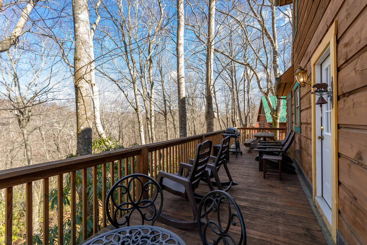 A wooden deck overlooks a scenic expanse of trees, equipped with classic rocking chairs for enjoying the peaceful mountain surroundings. The arrangement invites relaxation and quiet moments of wildlife watching or stargazing after a day outdoors.