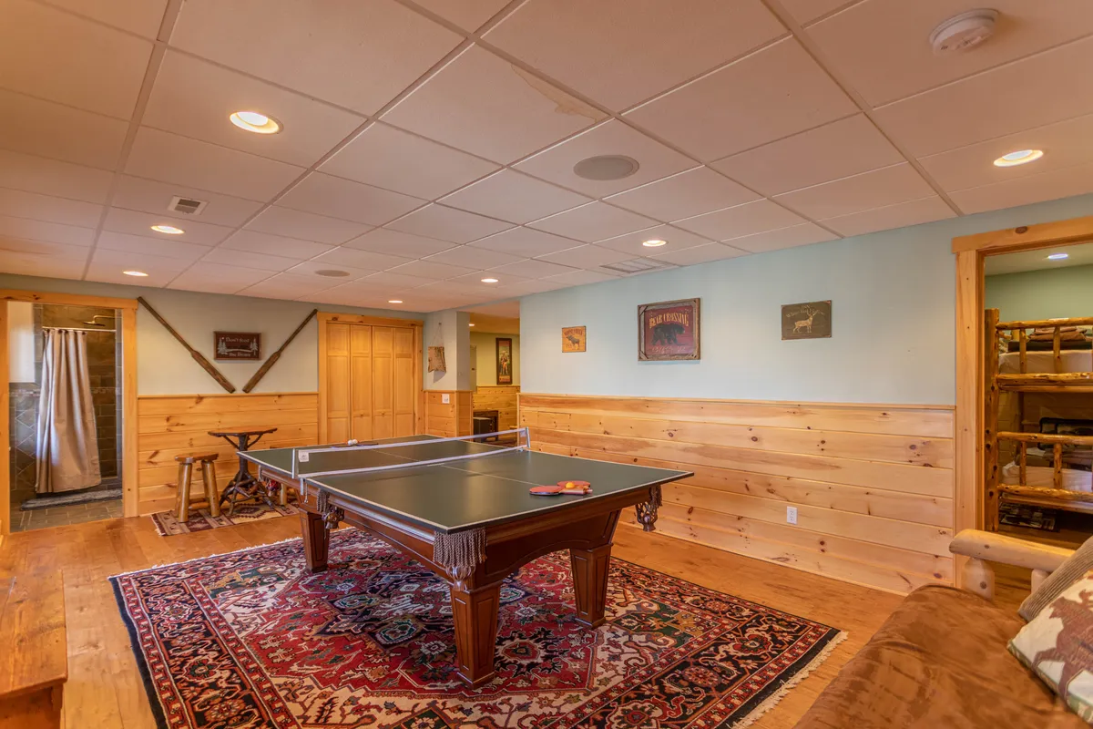A game room scene with a ping pong table set atop a cozy area rug, accented by warm wooden paneling and playful artwork on the walls. The inviting atmosphere is perfect for friendly competitions and gatherings.