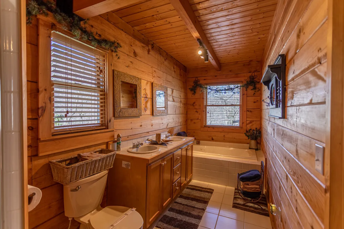 Bathroom featuring a double sink vanity, a soaking tub, wooden walls, and abundant natural light from the windows—suggesting a spa-like, relaxing environment.
