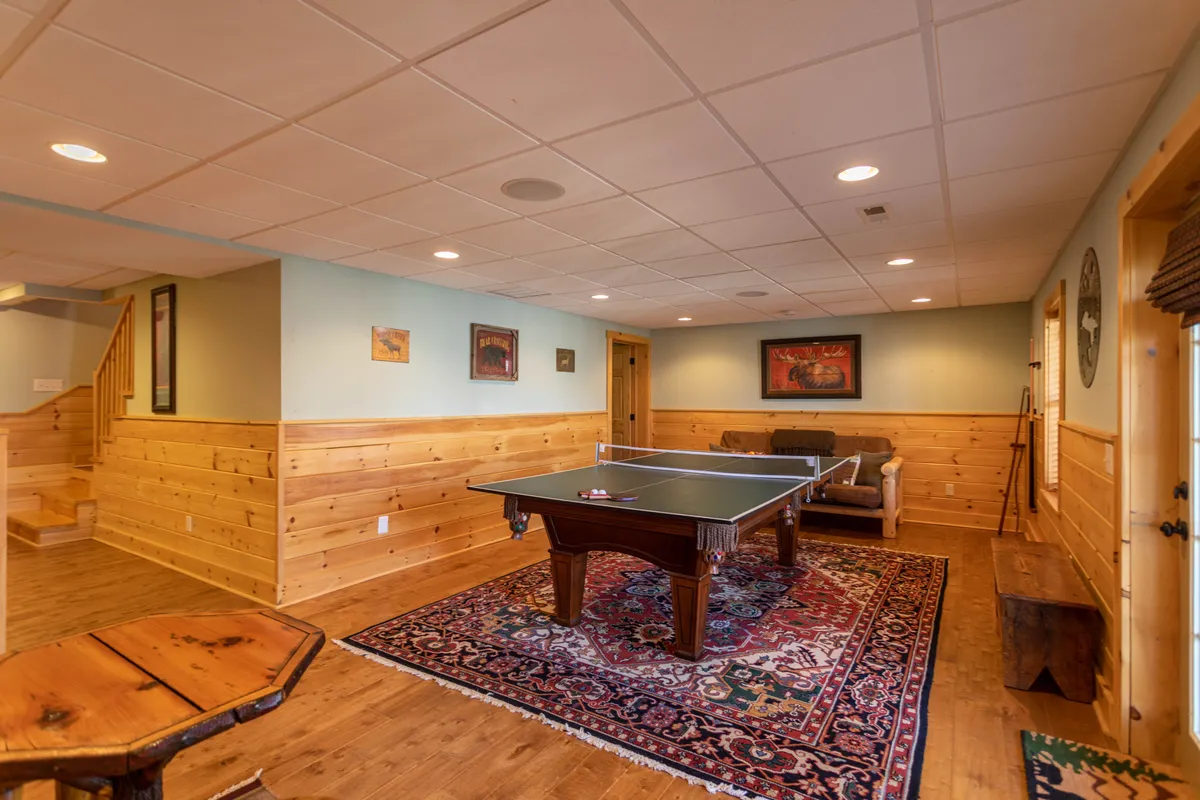 A friendly, inviting game room featuring a ping pong table, a wooden bench, a cozy sofa, and a colorful rug. The space is designed for fun, laughter, and memorable family competitions, providing an indoor retreat for all ages.